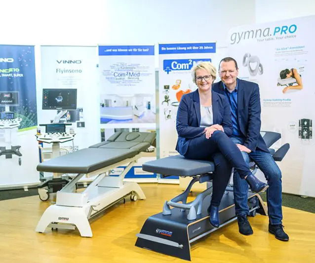 com2med Geschäftsführer Christin und Jens-Uwe Mühlan sitzen auf einer medizinischen Liege.