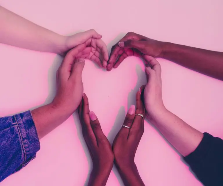 Hände vor rosa Hintergrund formen ein Herz.