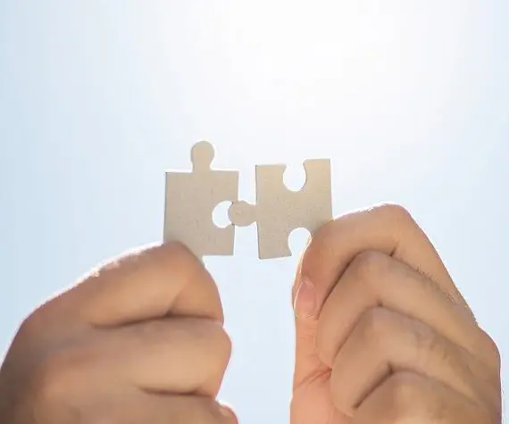 Zwei Hände halten Puzzleteile in den blauen Himmel.